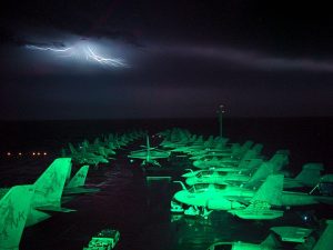 STORIA-MARINA-US-PORTAEREI-US_Navy_021102-N-0000W-001_Lightning_fills_the_horizon_and_lights_up_the_flight_deck_and_air_wing_aircraft_parked_on_the_ships_forward_elevator_and_bow
